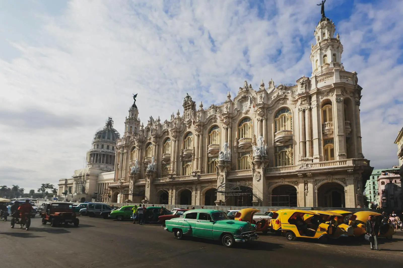 Photo by Mehmet Turgut Kirkgoz Vintage cars line the streets in front of a historic Cuban building in Havana, capturing the city's charm.