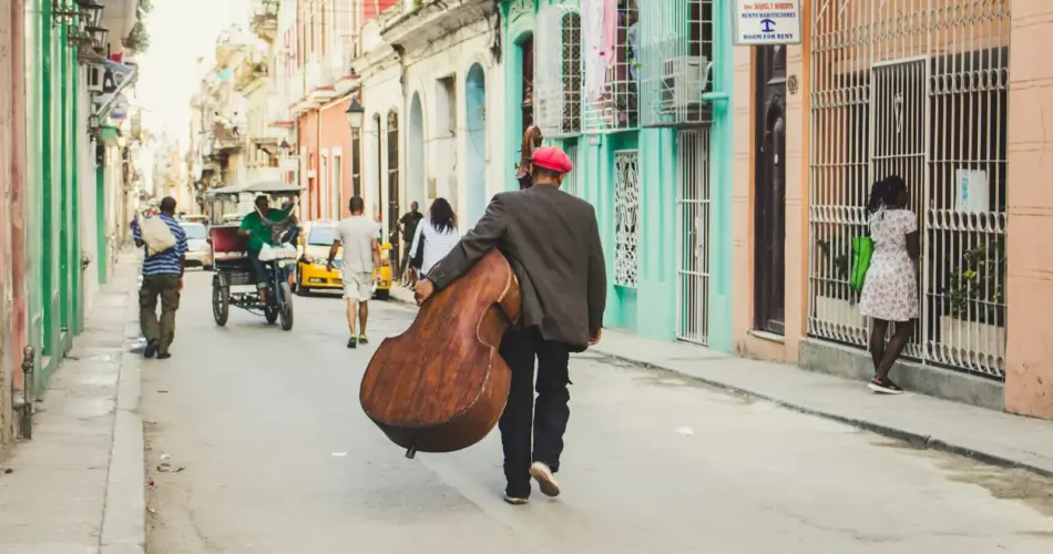 man carrying stringed instrument while walking the pavement during daytime